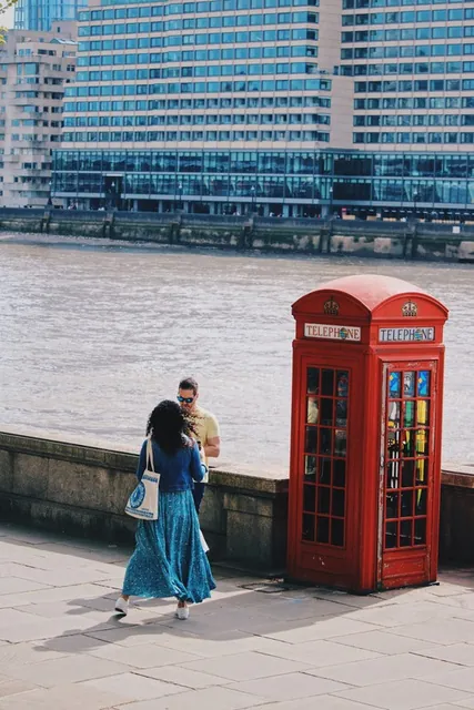 Mujer pasando junto a una cabina roja a orillas del Támesis