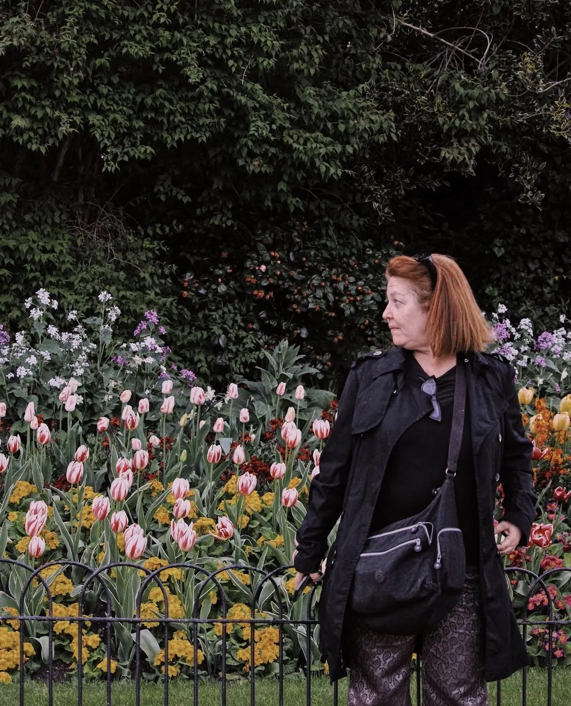 Mujer con gabardina negra frente a un parterre de tulipanes