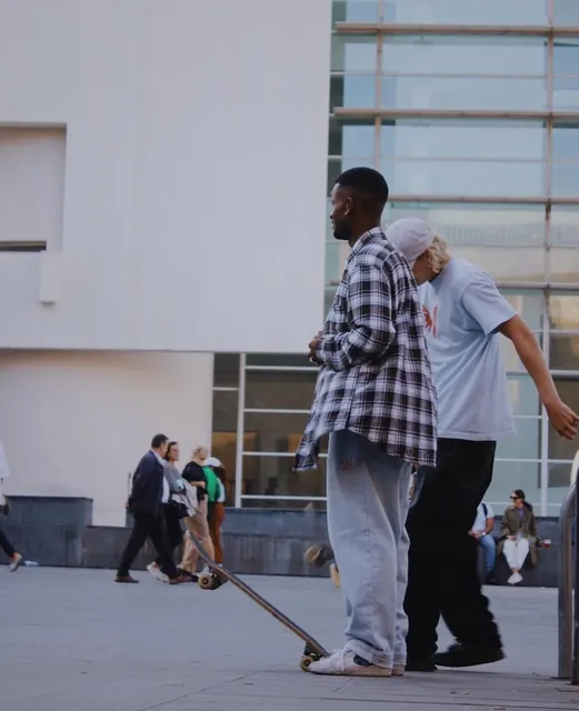 Dos hombres conversando con un skate en la plaza