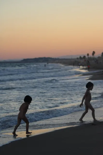 Dos niños corriendo por la orilla al atardecer