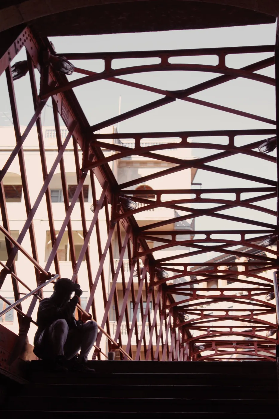 Silueta sentada en la escalera de un puente de hierro rojo