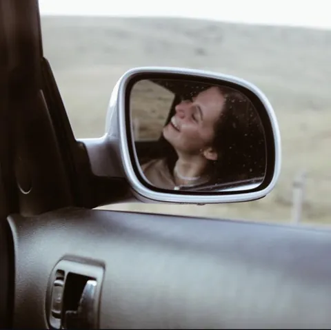 Chica sonriendo reflejada en el retrovisor de un coche