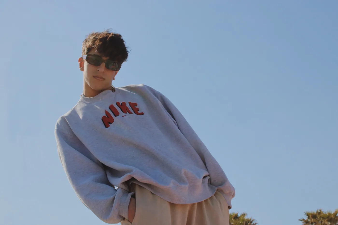 Chico con gafas de sol y sudadera gris contra el cielo azul